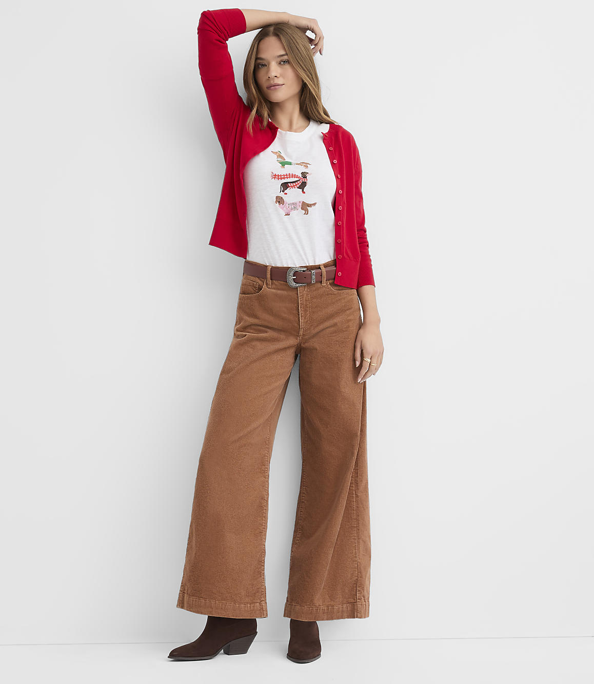 A woman wearing a red cardigan, a white graphic t-shirt, and brown wide-leg corduroy pants stands against a plain white background.