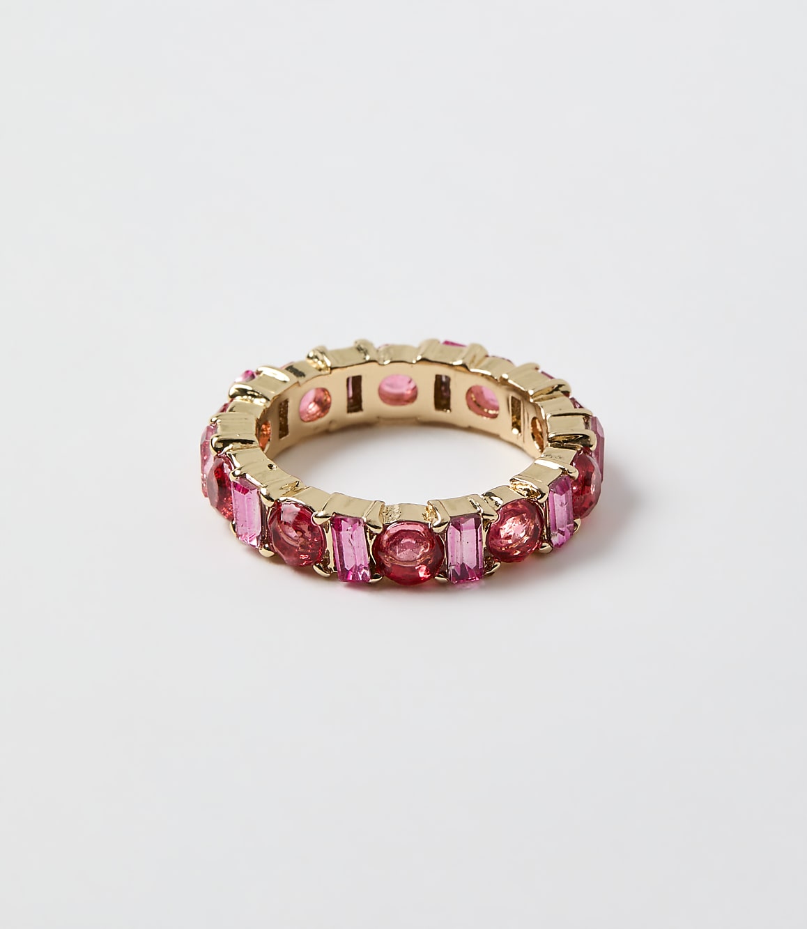 A gold ring set with pink gemstones rests on a plain white background.
