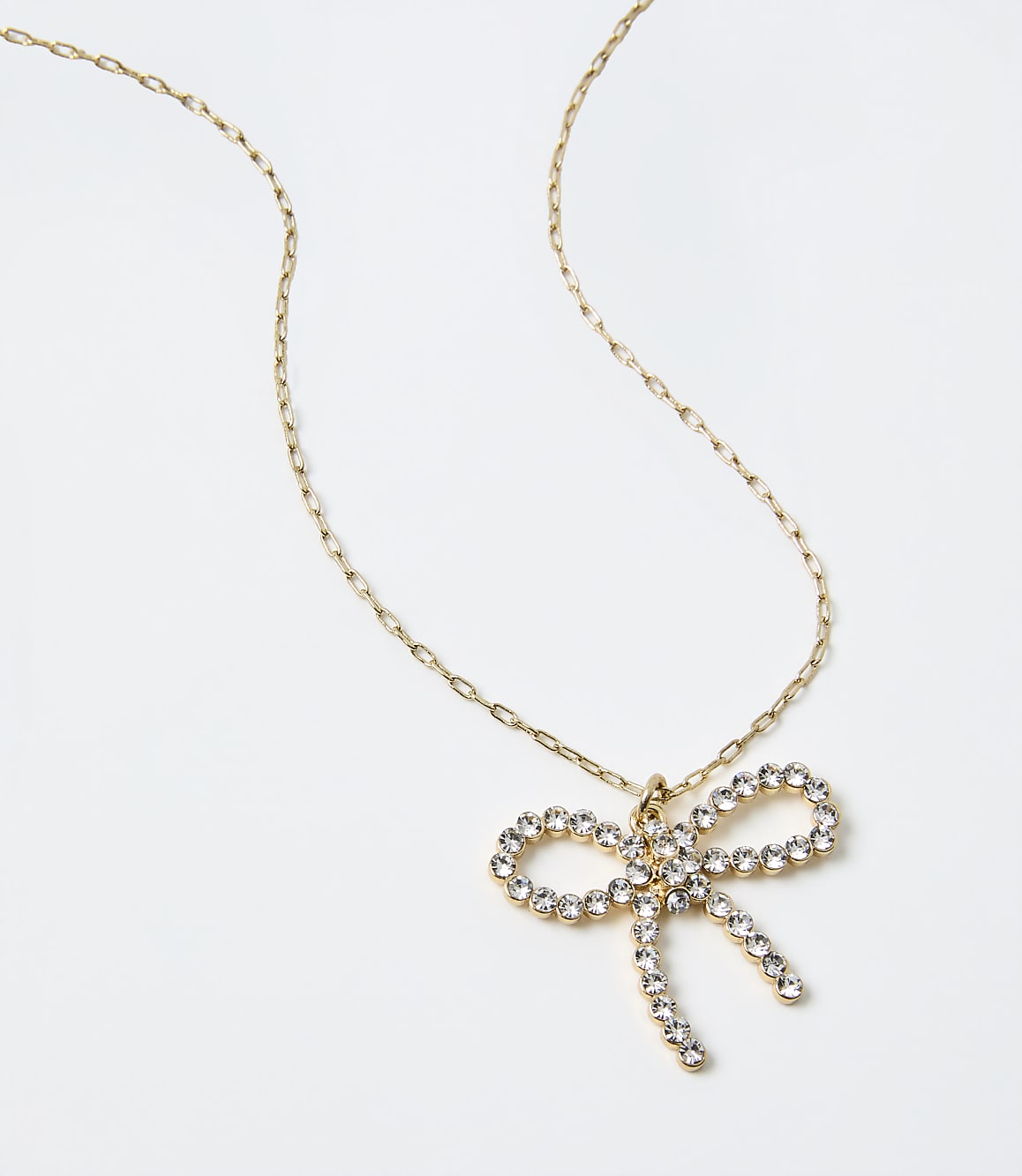 A gold chain necklace with a sparkling bow-shaped crystal pendant rests on a plain white background.