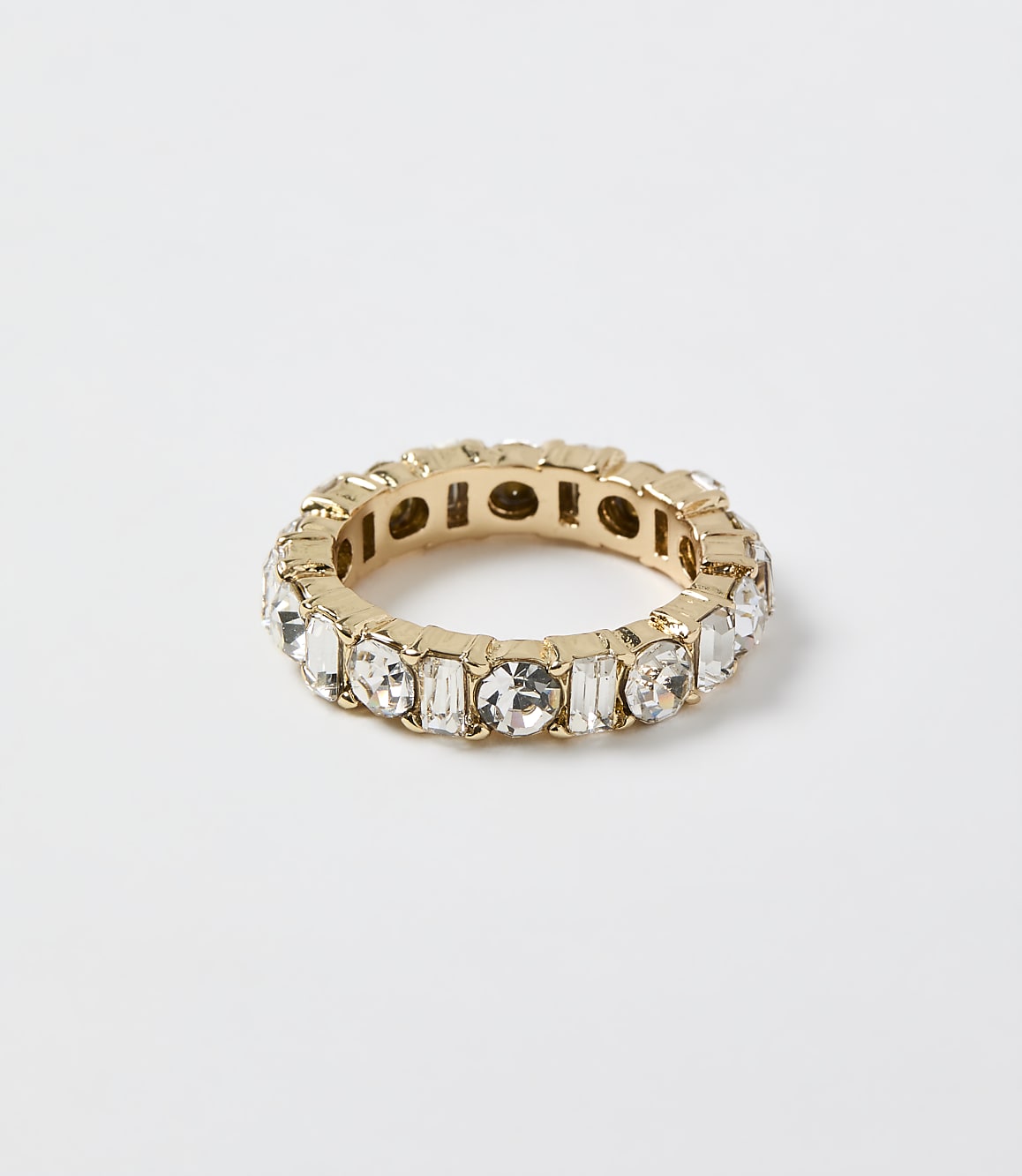A gold ring set with clear crystals rests on a plain white background.