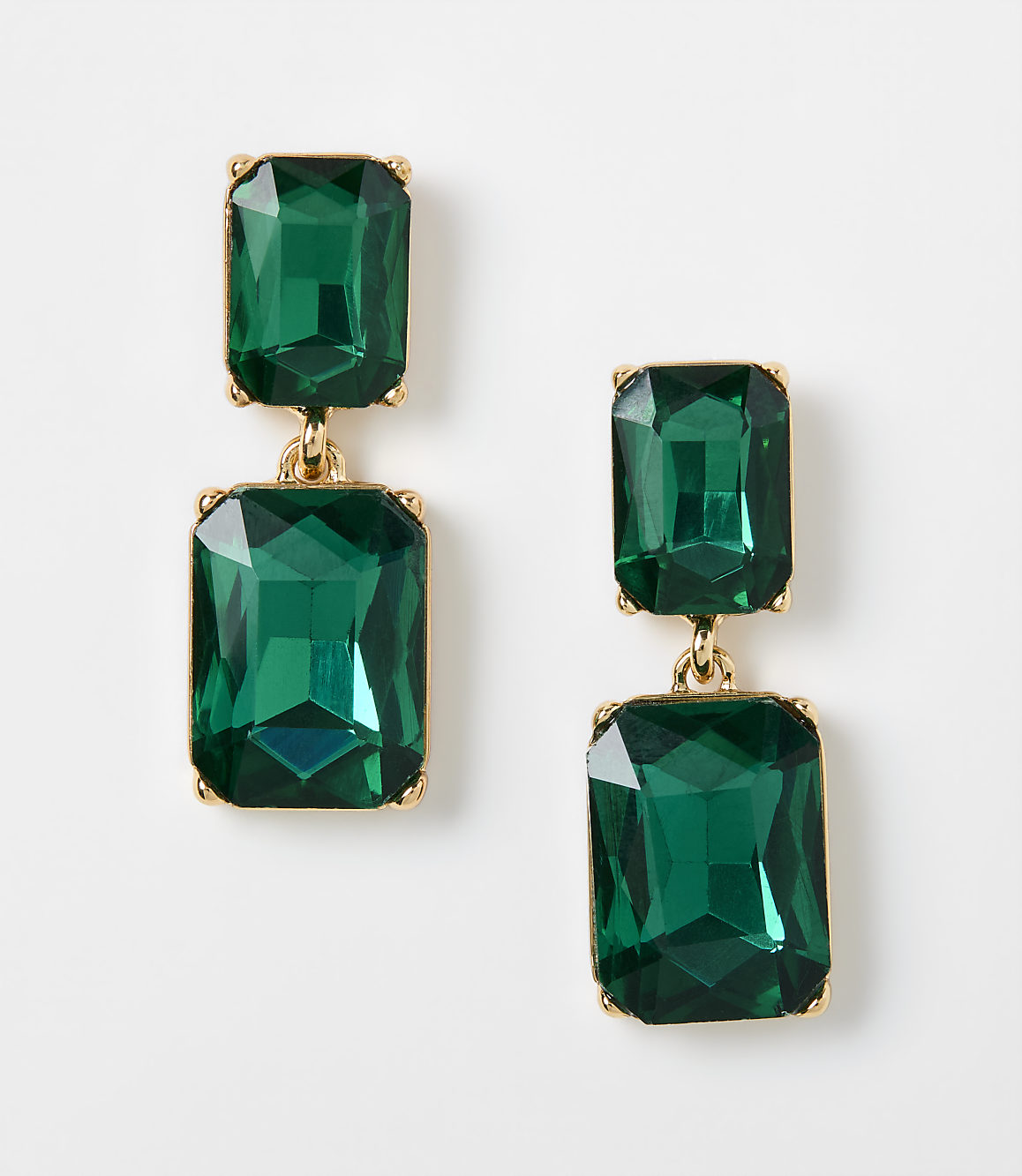 Two pairs of emerald green rectangular drop earrings with gold settings rest on a plain white background.