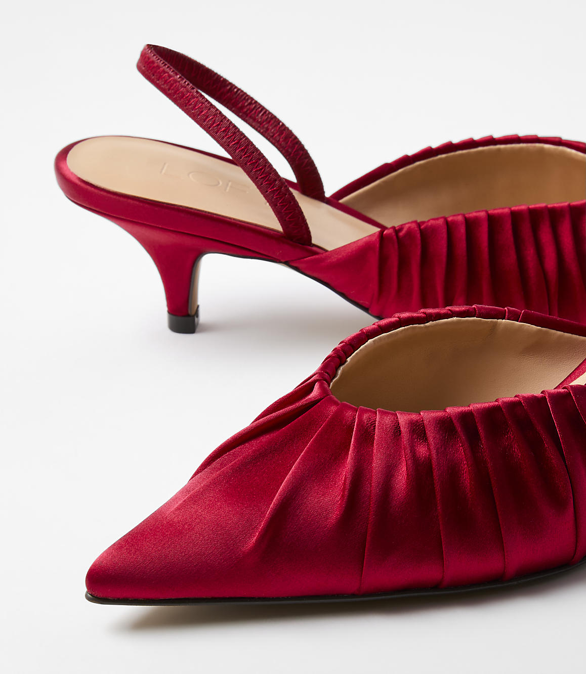 A pair of red satin slingback heels with pleated detailing sits against a plain white background.