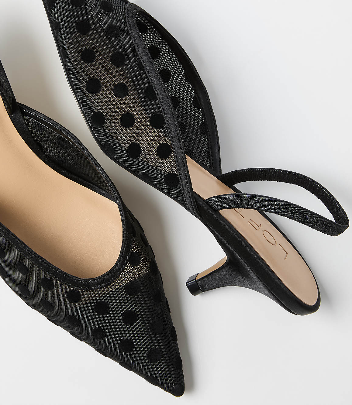 Two black polka-dot mesh pointed-toe heels rest on a plain white background.