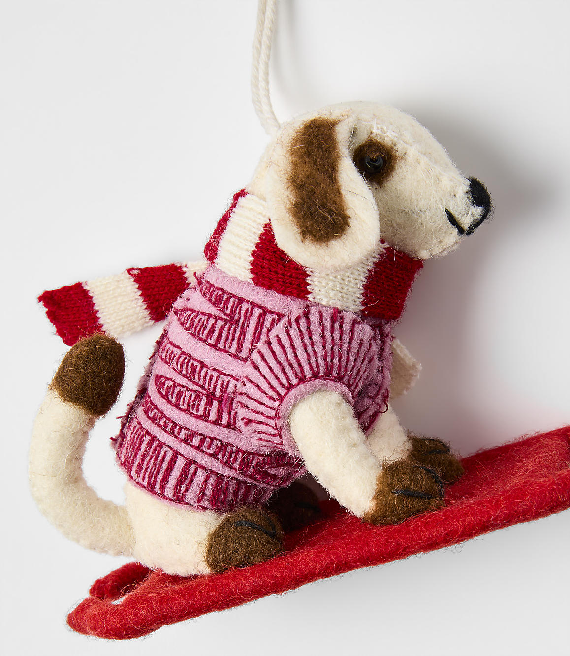 A small felt dog wearing a pink and red striped sweater stands on a red sled against a plain white background.
