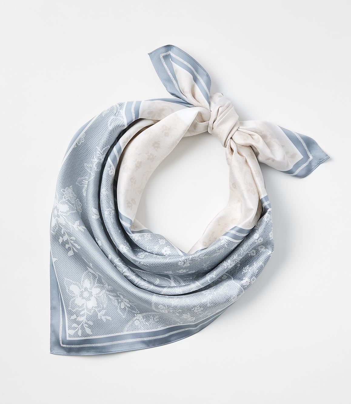 A light blue and white patterned silk scarf is tied in a knot against a plain white background.
