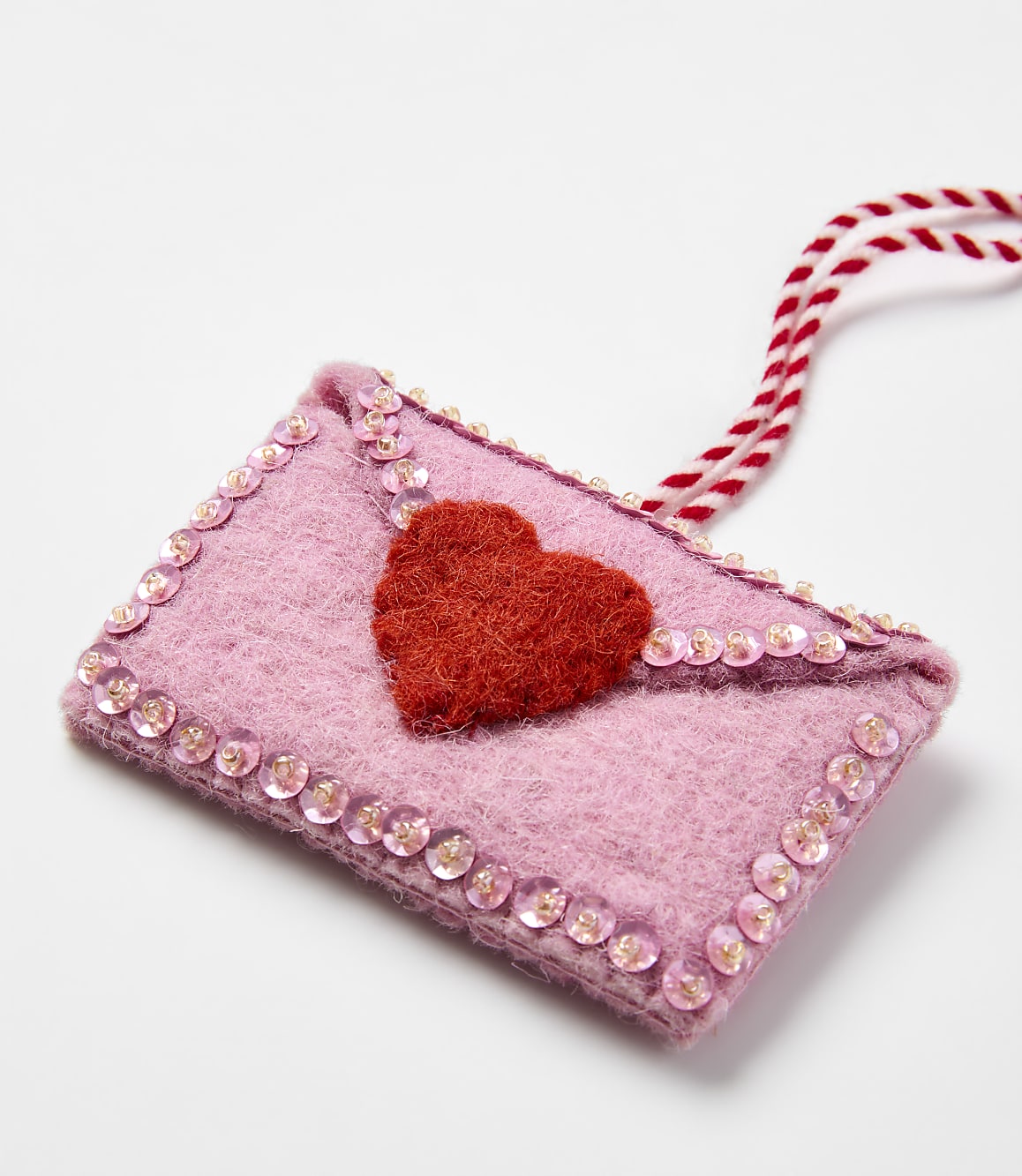 A pink felt envelope with a red heart and sequins sits on a plain white background.