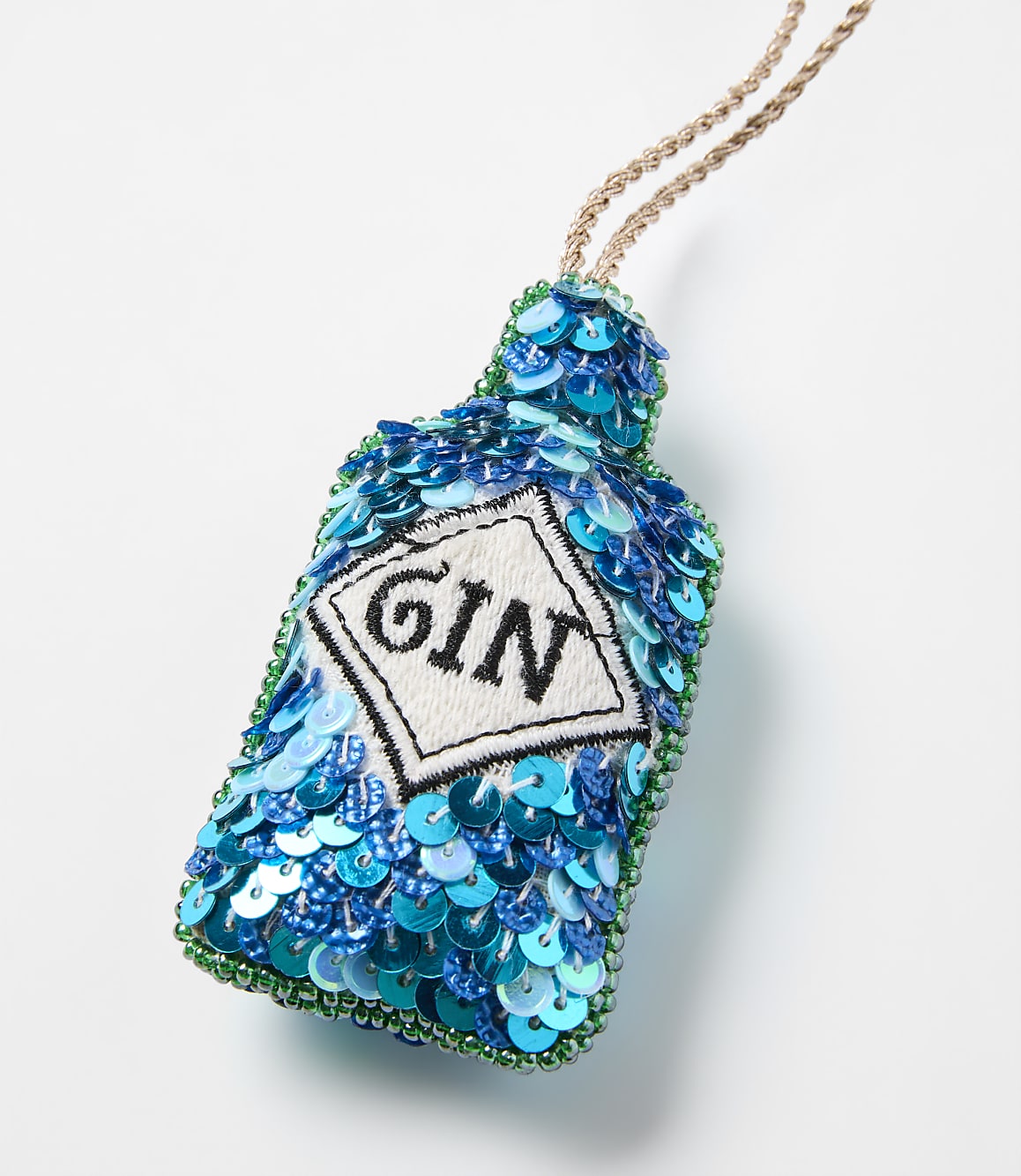A blue and green sequined gin bottle ornament with a white label hangs against a plain white background.