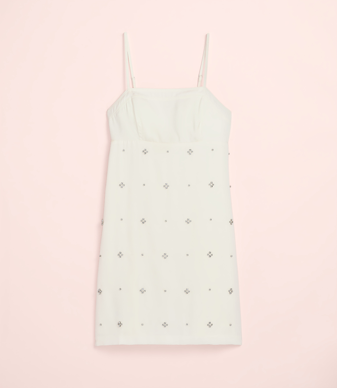 A white mini dress with silver embellishments is centered against a solid light pink background.