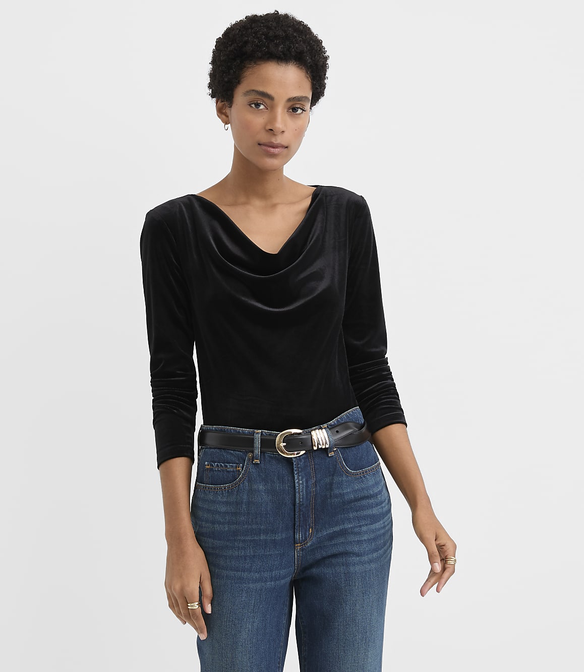 A woman wearing a black velvet top and blue jeans stands against a plain white background.