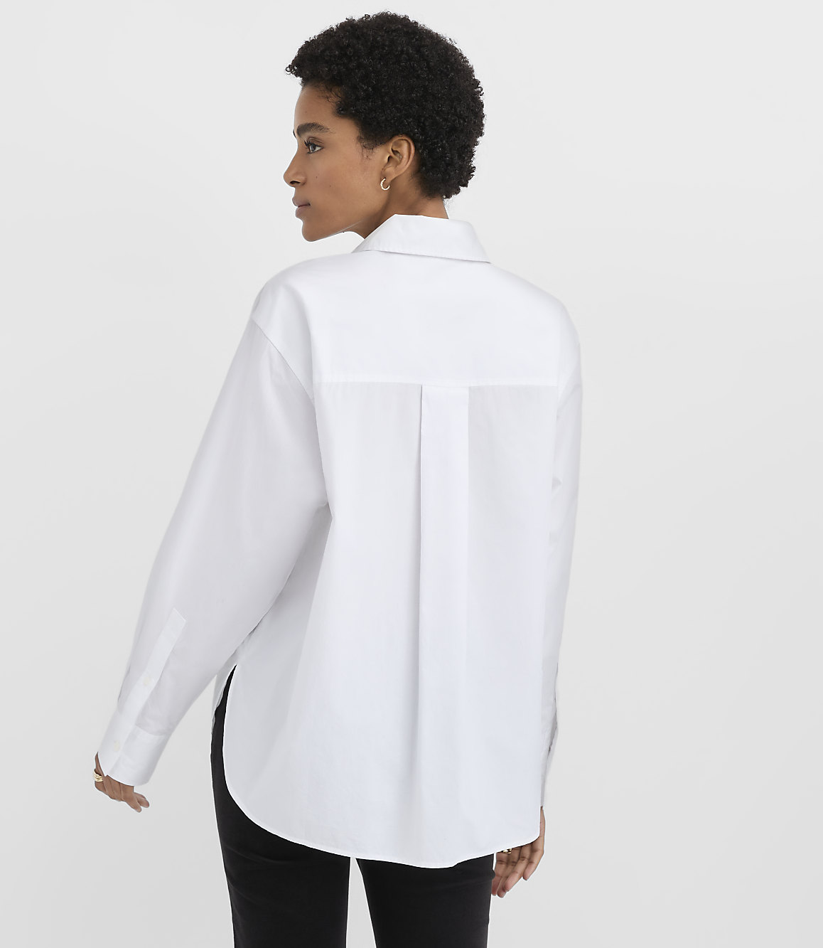 A woman wearing a white oversized button-down shirt and black pants stands against a plain white background.
