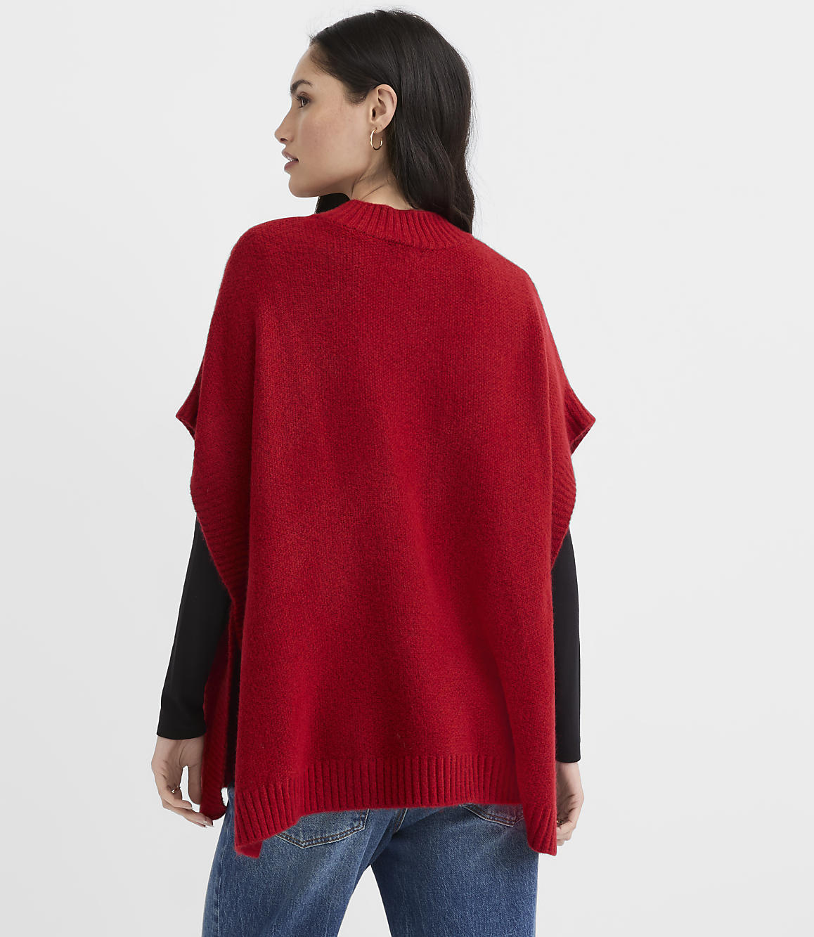A woman wearing a red poncho and blue jeans stands against a plain white background.