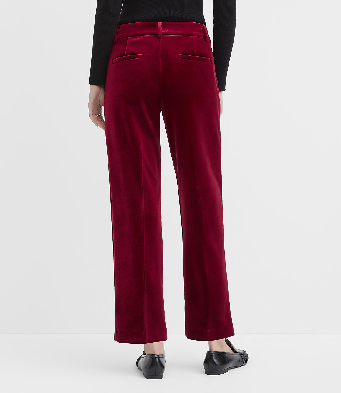 A person wearing a black top and red velvet trousers stands against a plain white background.