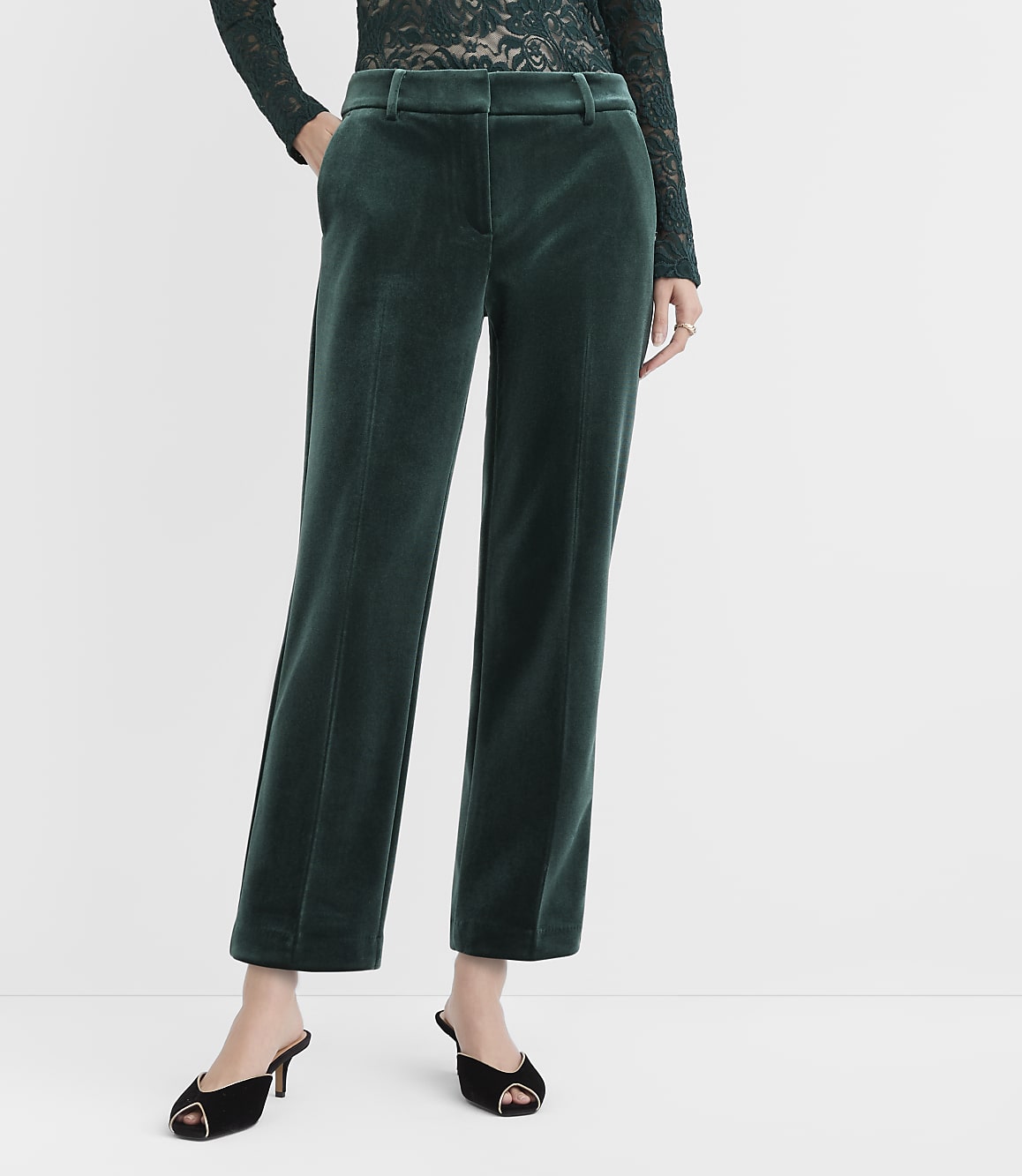 A person wears dark green velvet wide-leg trousers and black open-toe heels against a plain white background.