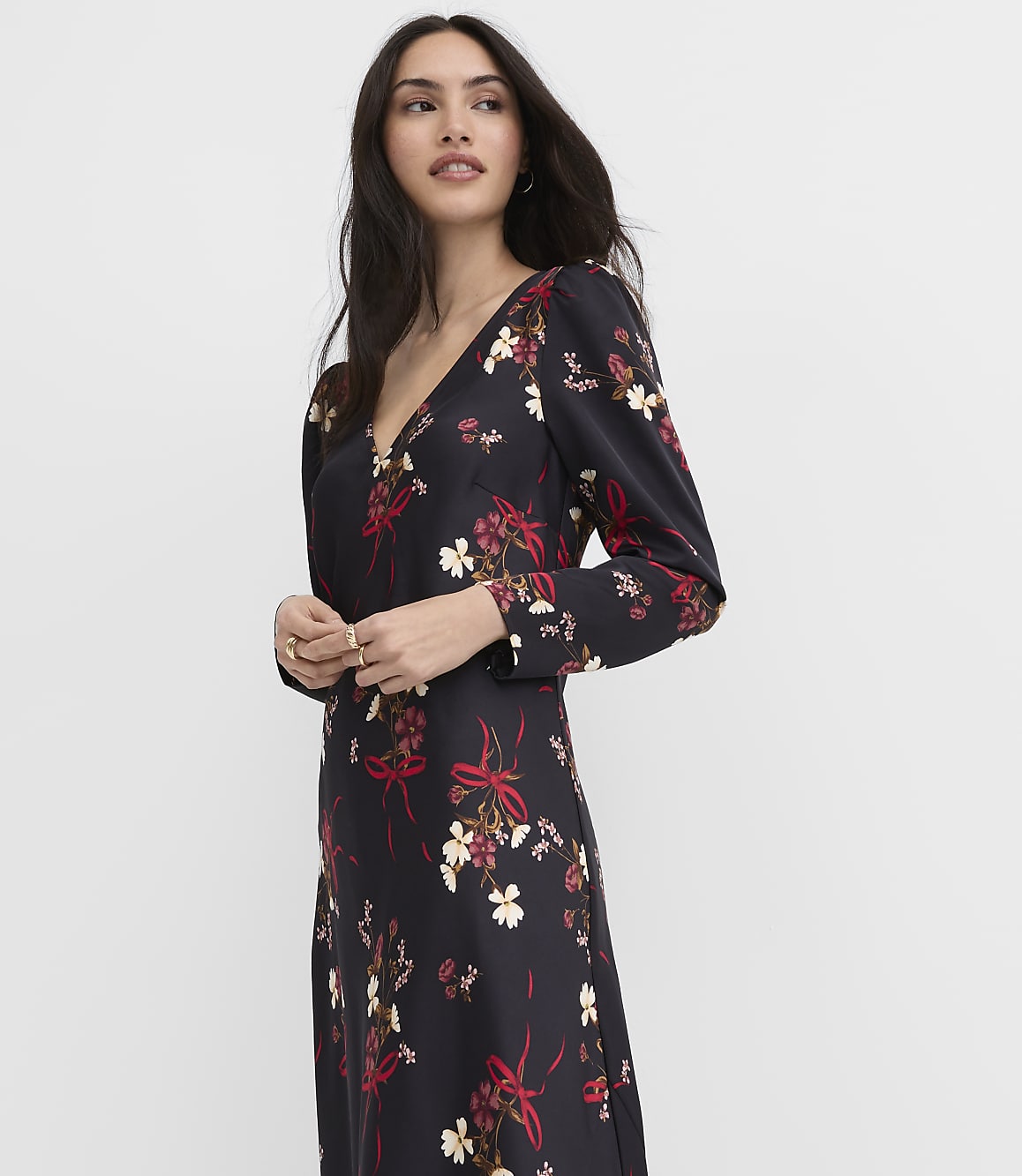 A woman wearing a black floral dress stands against a plain white background.