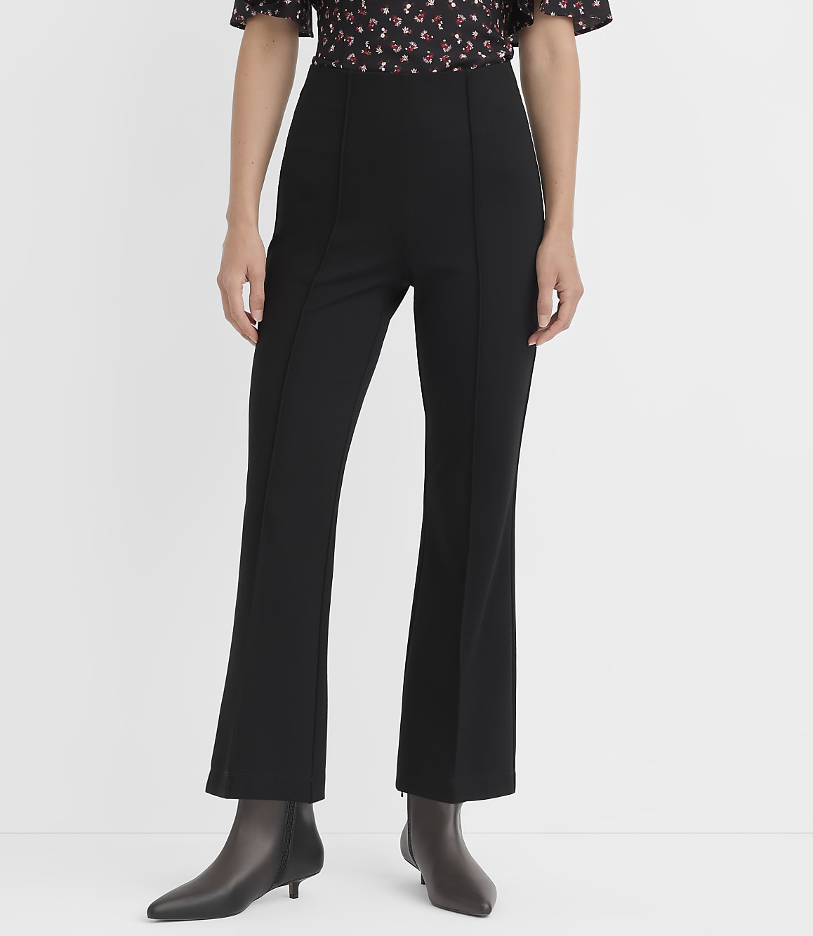 A person stands in black flared pants and pointed-toe boots against a plain white background.