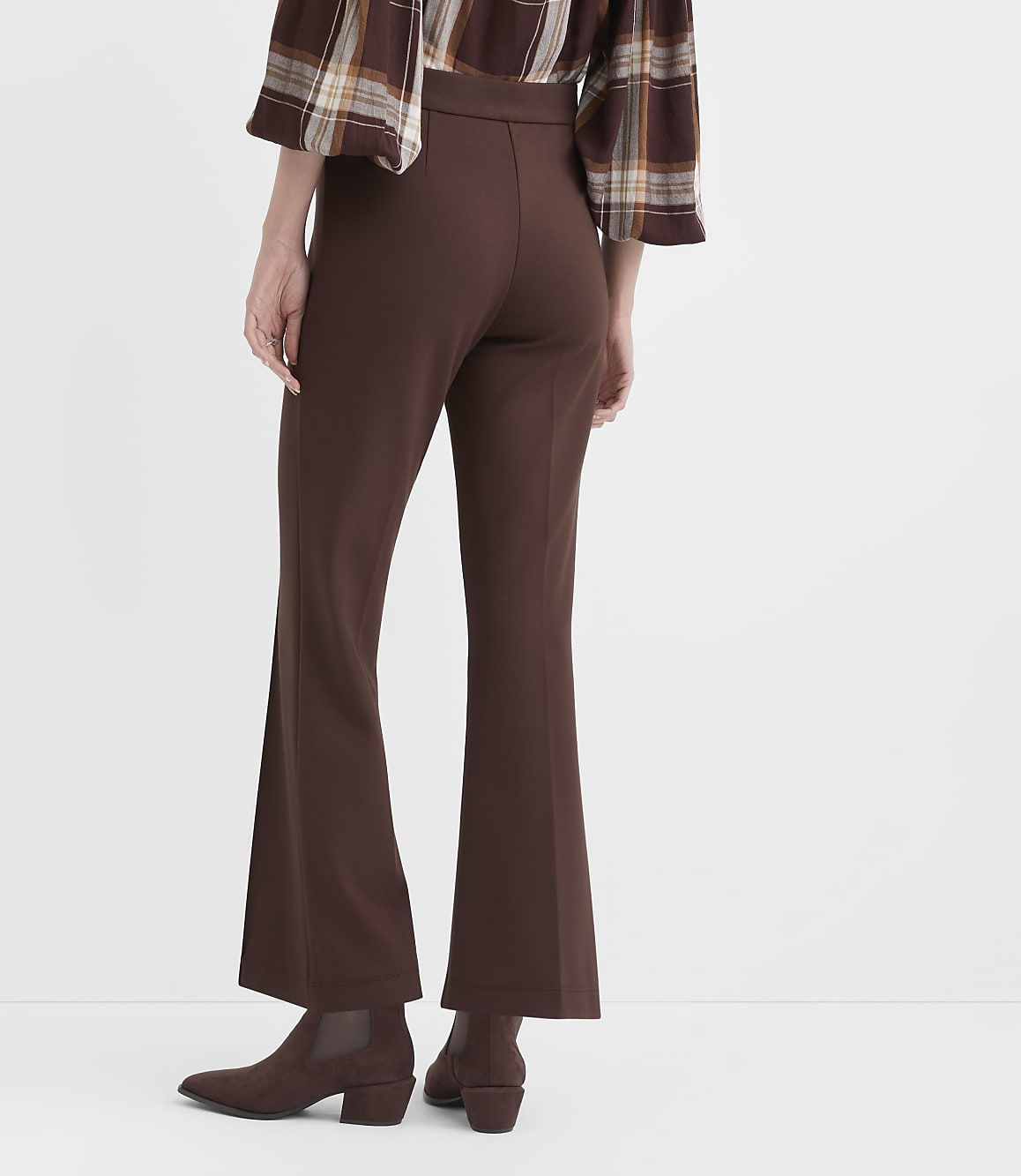 A person wearing brown flared pants and boots stands against a plain white background.