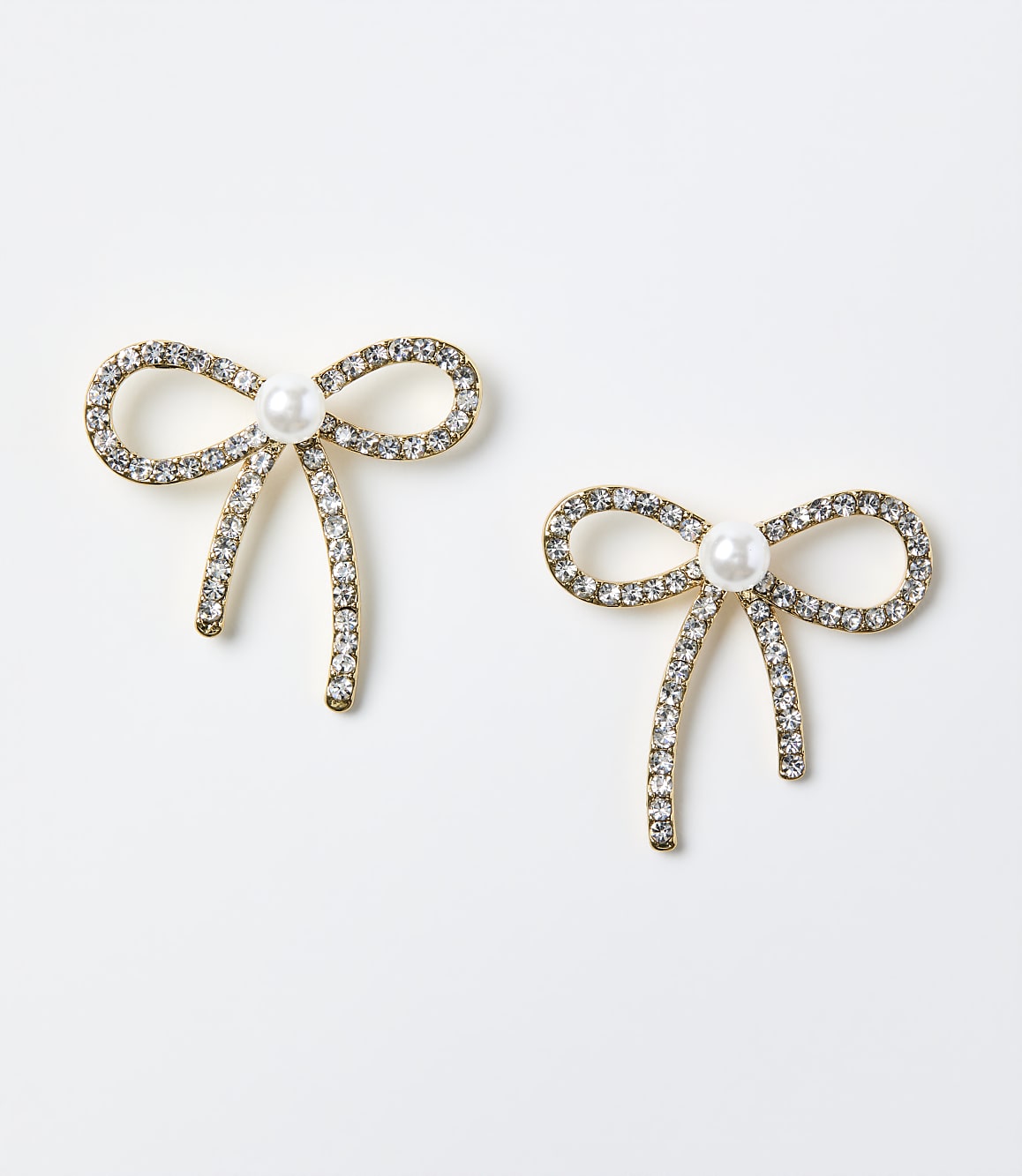 Two gold-toned bow earrings adorned with crystals and a central pearl rest on a plain white background.