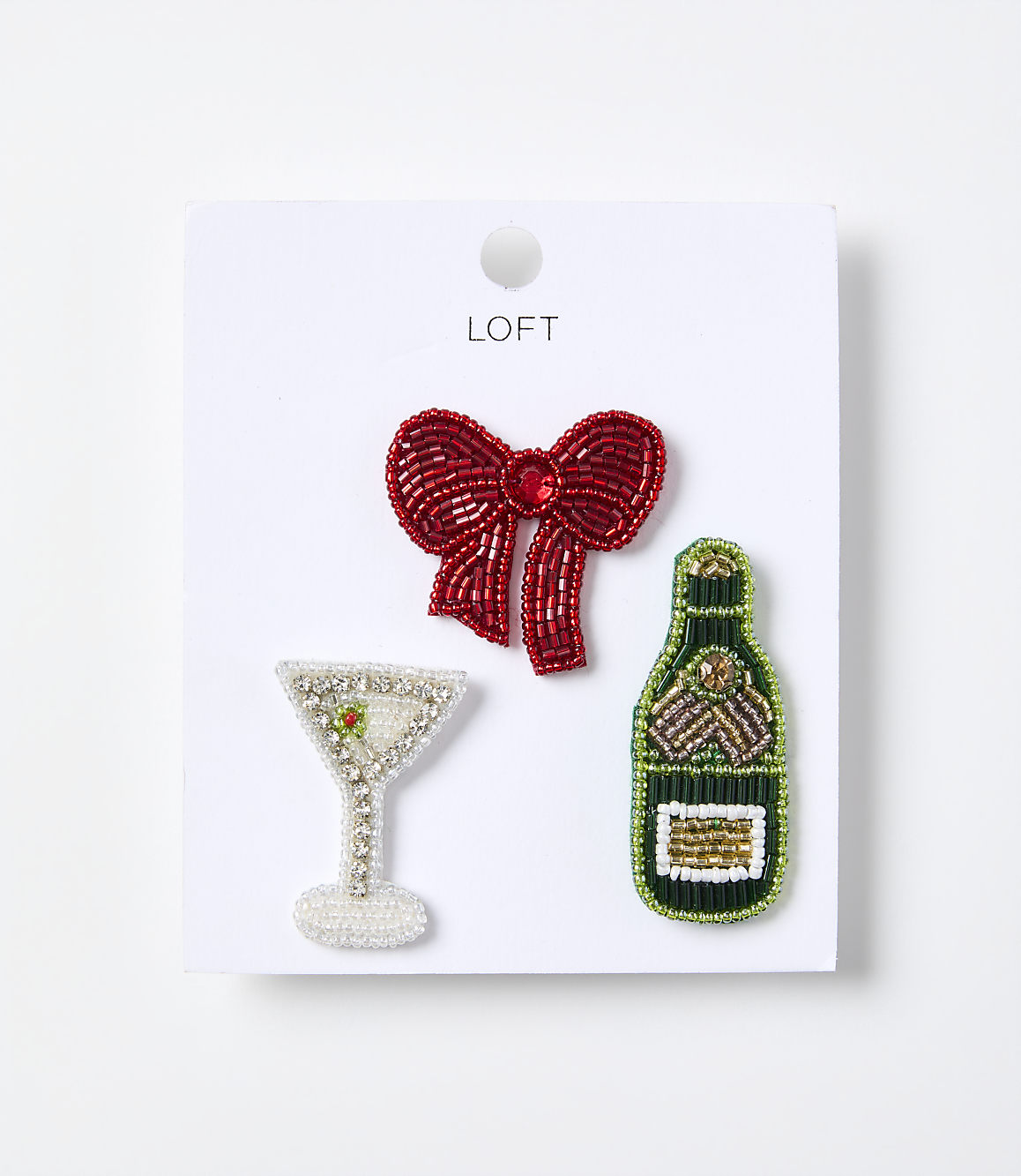 Three beaded brooches&mdash;a red bow, a champagne glass, and a green bottle&mdash;are displayed on a white card against a plain white background.