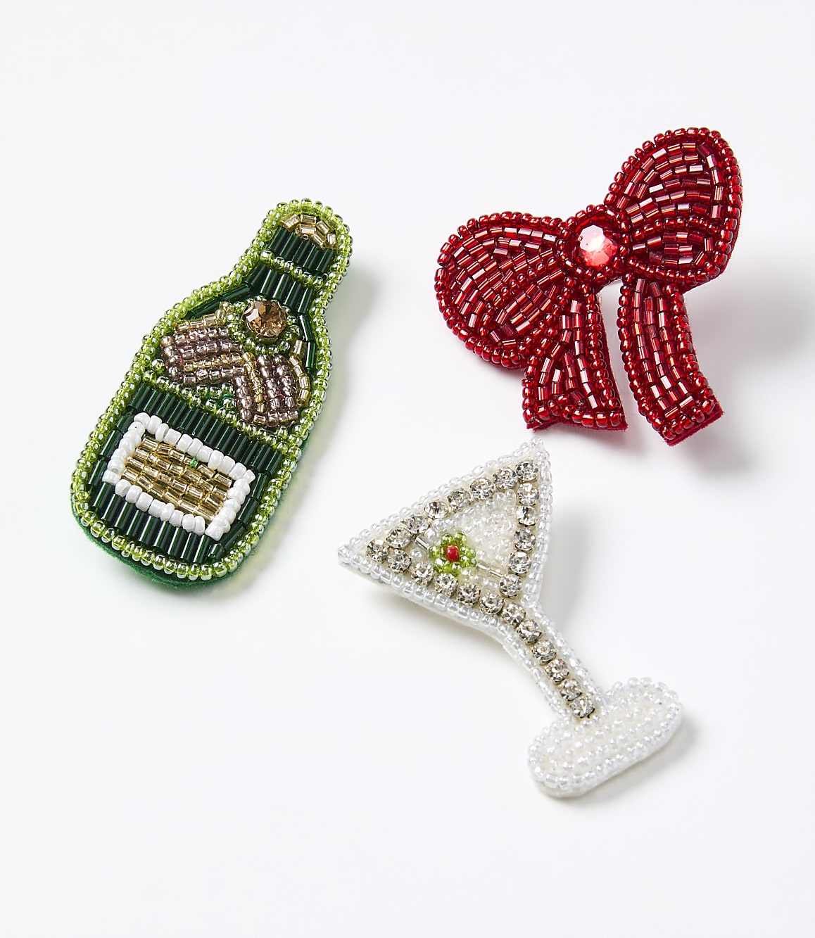 Beaded brooches shaped like a champagne bottle, a red bow, and a martini glass are arranged on a plain white background.