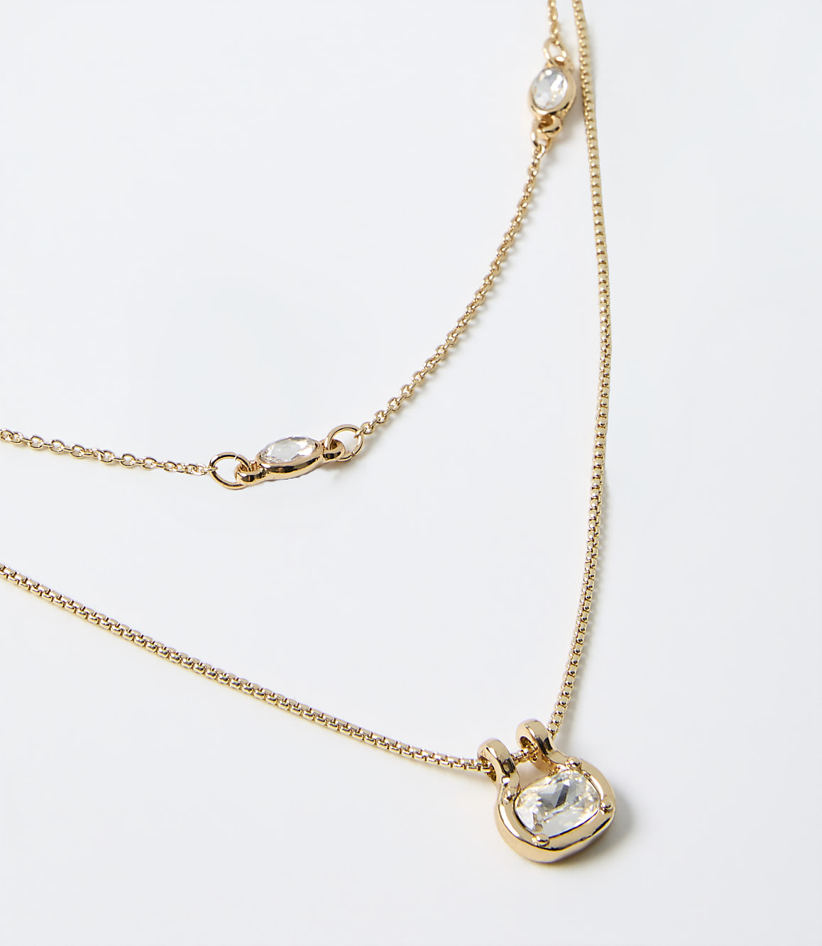 Two gold layered necklaces with clear gemstones rest on a plain white background.