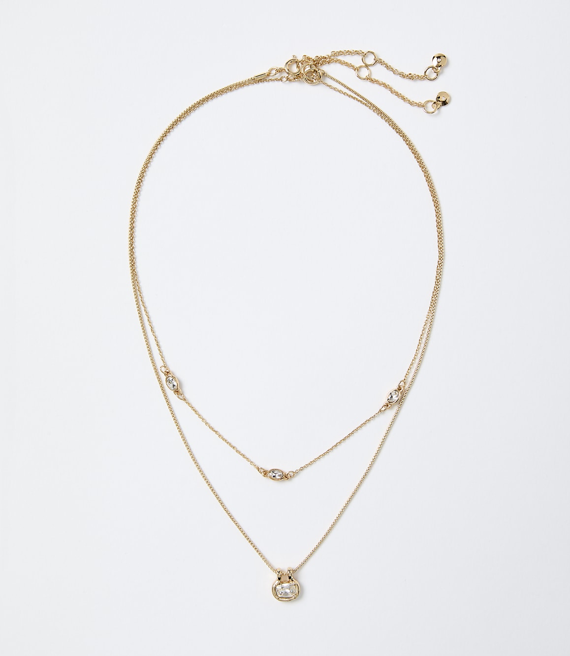 A layered gold necklace with small sparkling crystals rests against a plain white background.