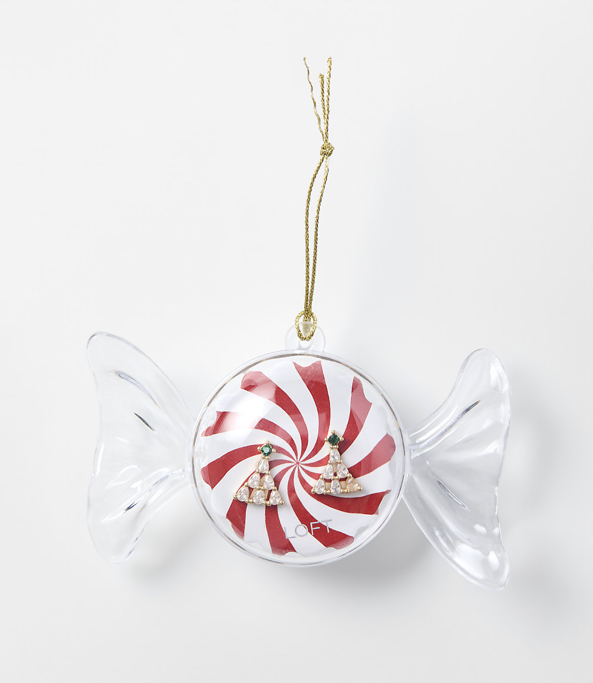 A pair of sparkling Christmas tree earrings sits inside a candy-shaped clear ornament with a red and white peppermint background, set against a plain white surface.