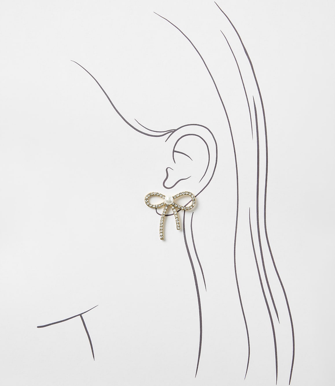 A gold bow-shaped earring with crystals sits on a simple line drawing of a woman's profile against a plain white background.