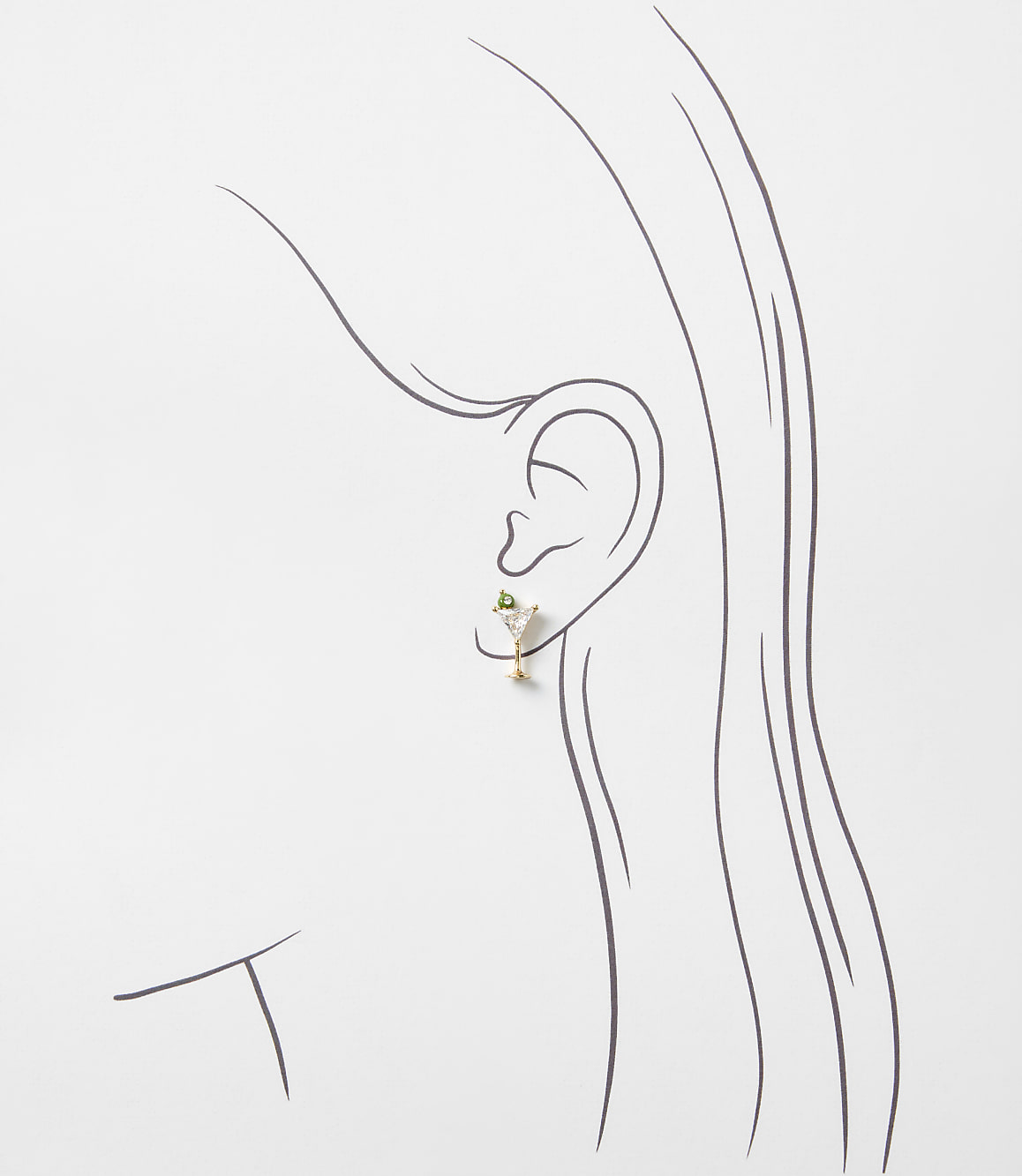 A small gold martini glass earring with a green gemstone sits on a minimalist line drawing of a woman's profile against a plain white background.