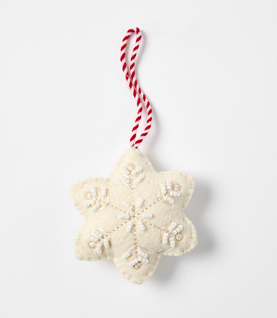 A cream-colored felt snowflake ornament with white bead accents and a red-and-white twisted string hangs against a plain white background.
