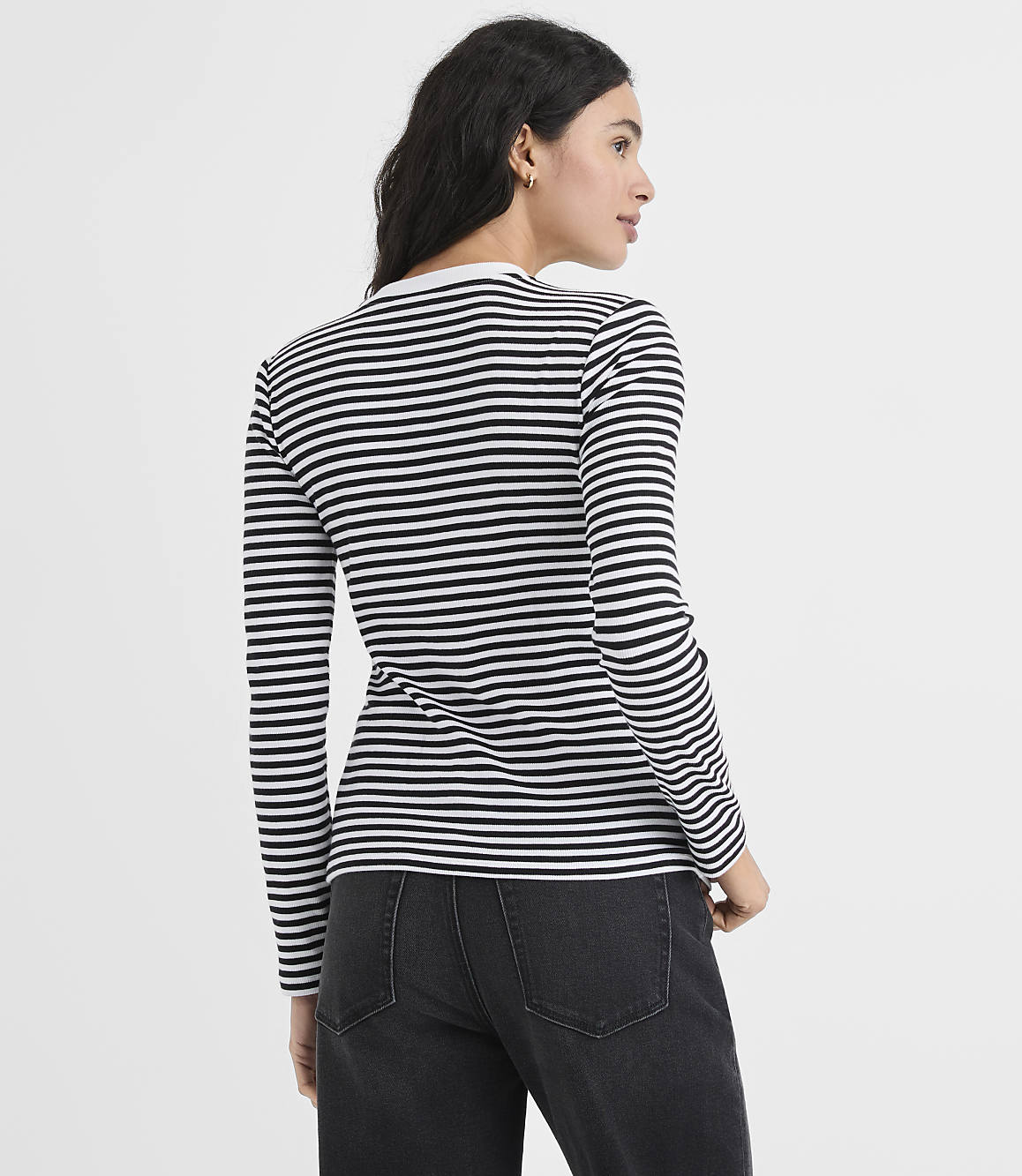 A woman wearing a black and white striped long-sleeve shirt and black pants stands against a plain white background.