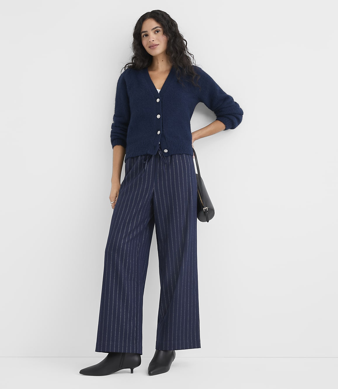 A woman wearing a navy blue cardigan and pinstriped wide-leg trousers stands against a plain white background.