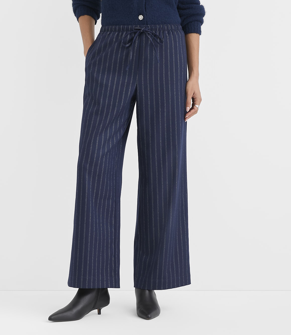 A person wearing navy blue pinstriped wide-leg pants and black pointed-toe heels stands against a plain white background.