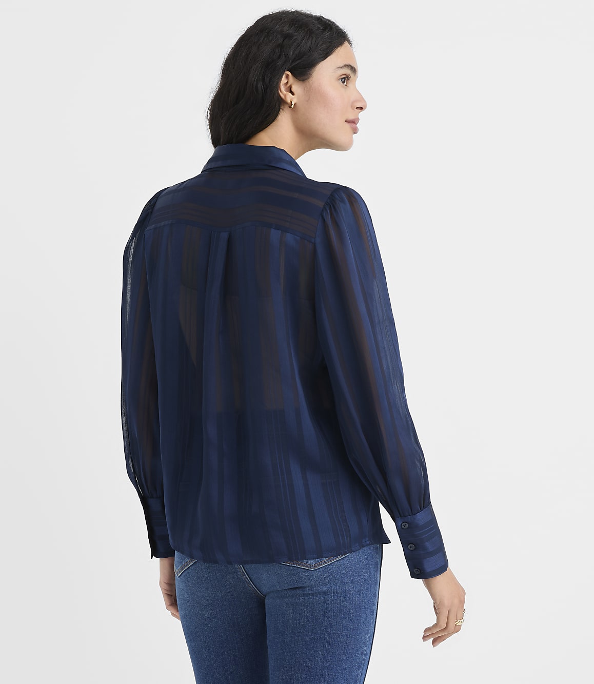 A woman wearing a navy blue striped blouse and blue jeans stands against a plain white background.