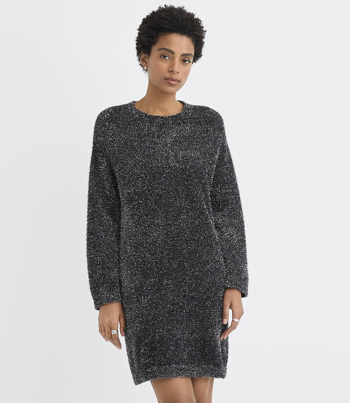 A woman wearing a shimmering dark grey knit dress stands against a plain white background.