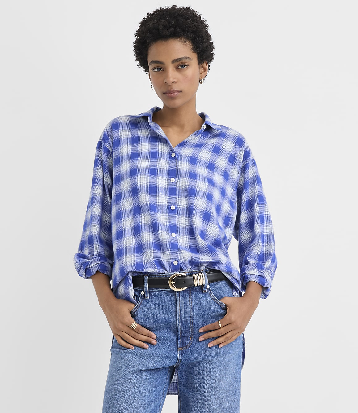 A woman wearing a blue plaid shirt and jeans stands against a plain white background.