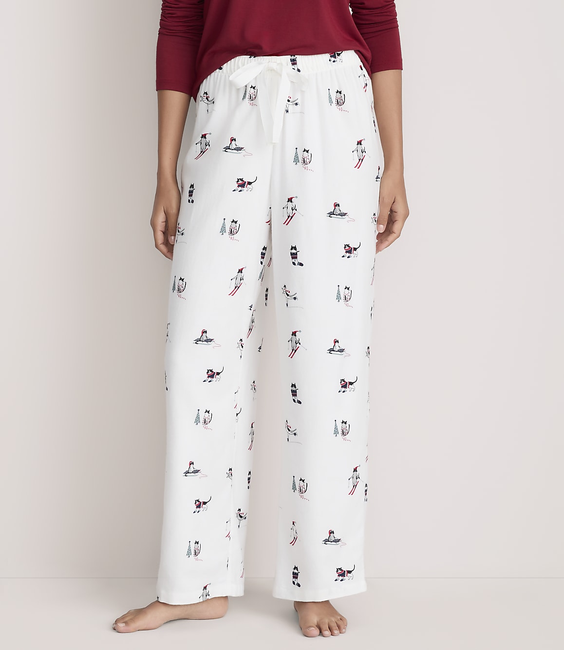 A person wearing a red shirt and white patterned pajama pants stands against a plain, light-colored background.