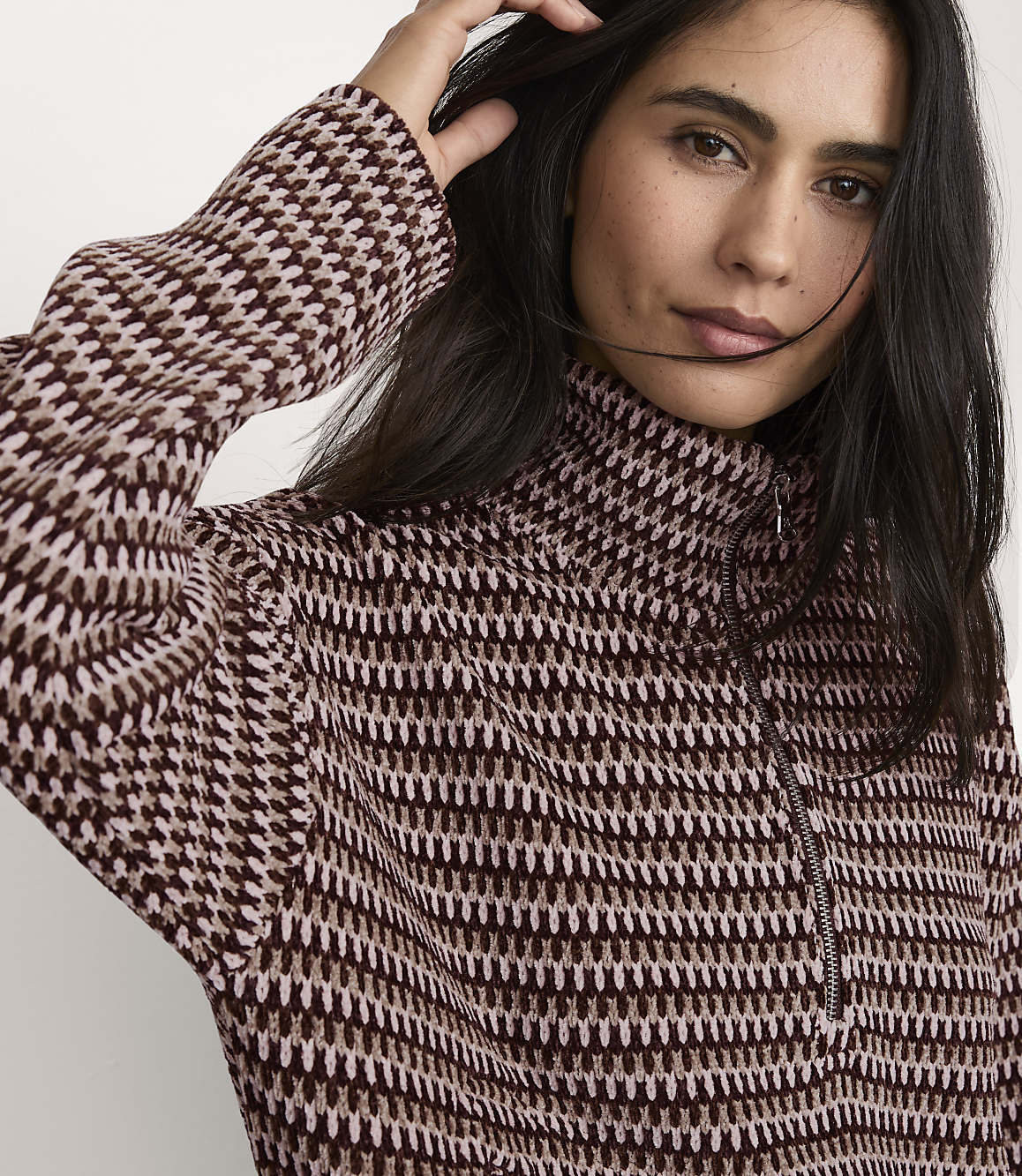 A woman wearing a patterned brown and cream quarter-zip sweater poses against a plain white background.