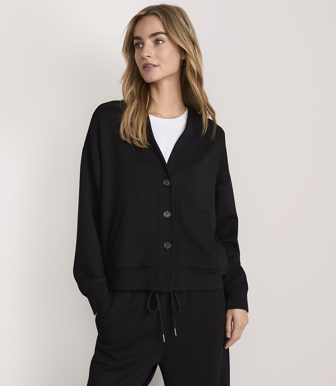 A woman wearing a black button-up jacket and matching pants stands against a plain, light-colored background.