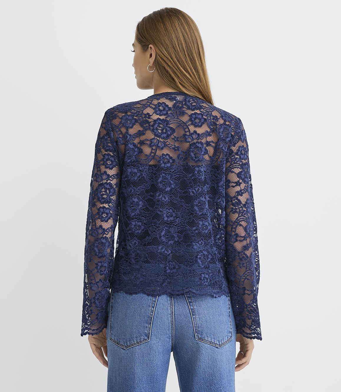 A woman wearing a navy blue lace top and blue jeans stands with her back to the camera against a plain white background.