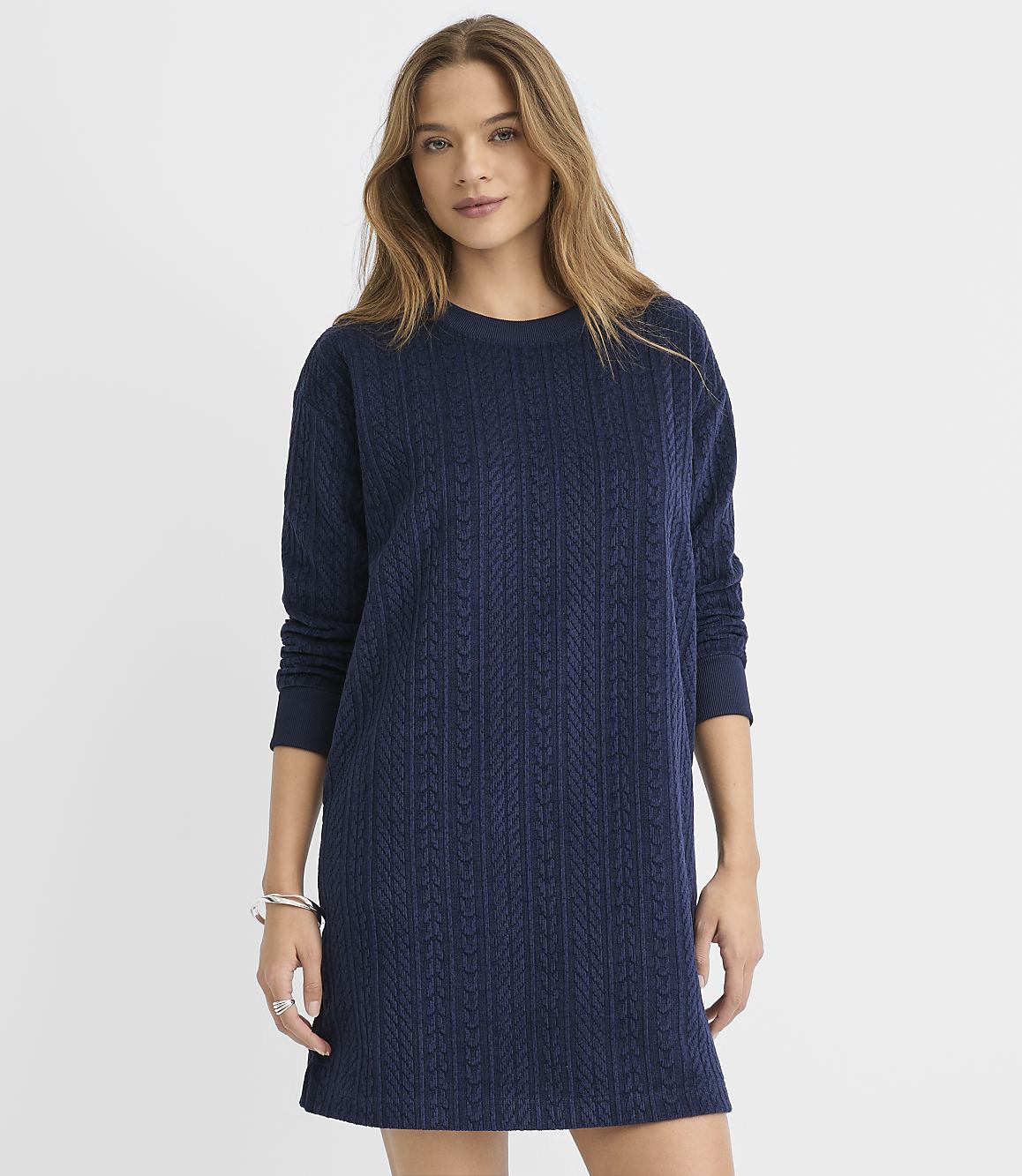 A woman wearing a navy blue cable-knit sweater dress stands against a plain white background.