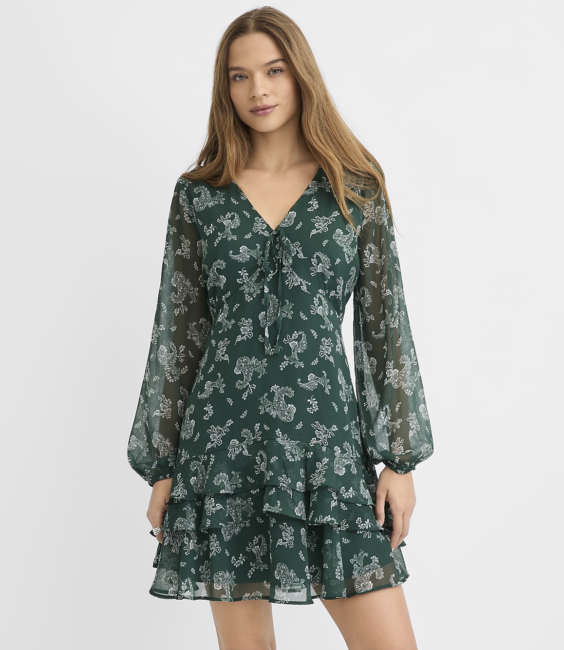 A woman wearing a green floral print dress stands against a plain white background.