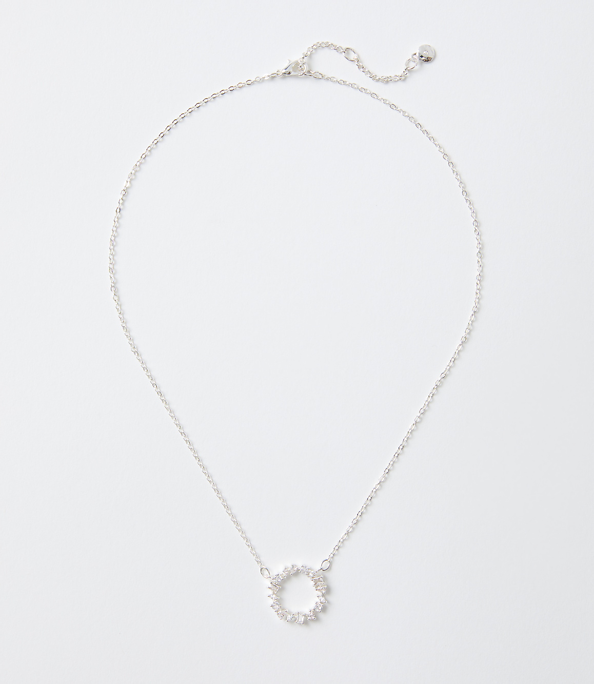 A silver necklace with a circular sparkling pendant rests on a plain white background.