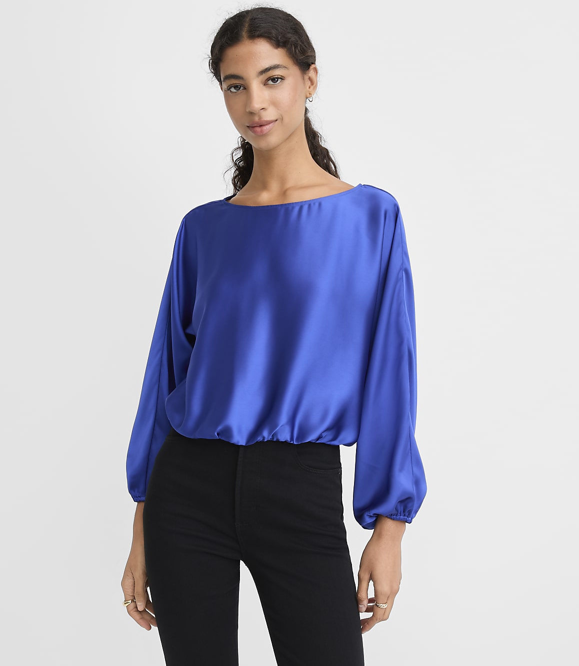 A woman wearing a royal blue satin blouse and black pants stands against a plain white background.