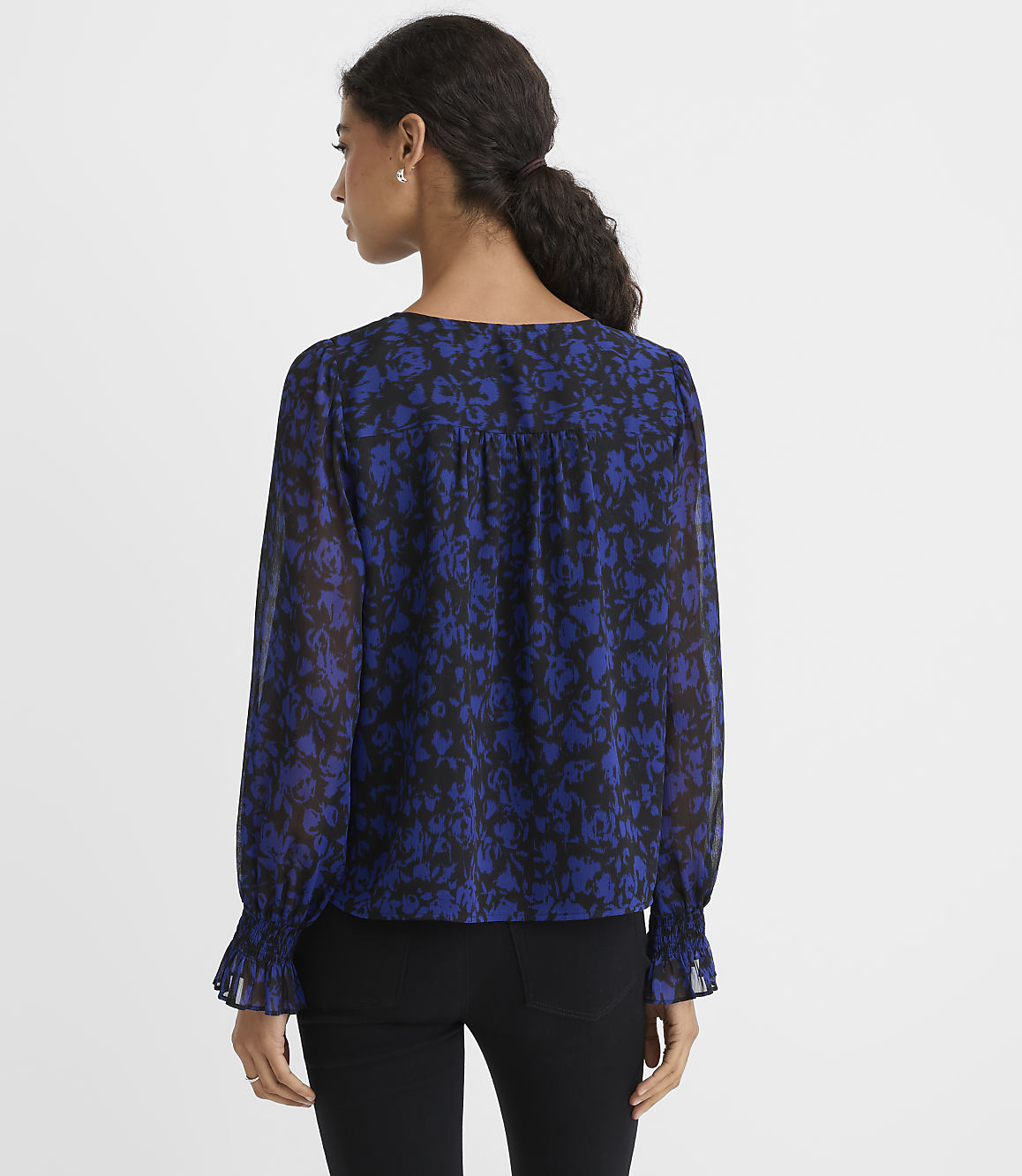 A woman wearing a blue and black floral print blouse and black pants stands against a plain white background.