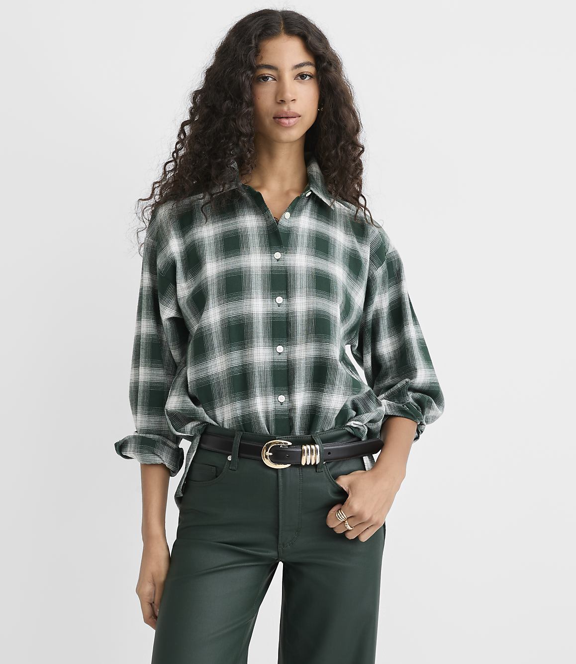 A woman wearing a green plaid shirt and dark green leather pants stands against a plain white background.