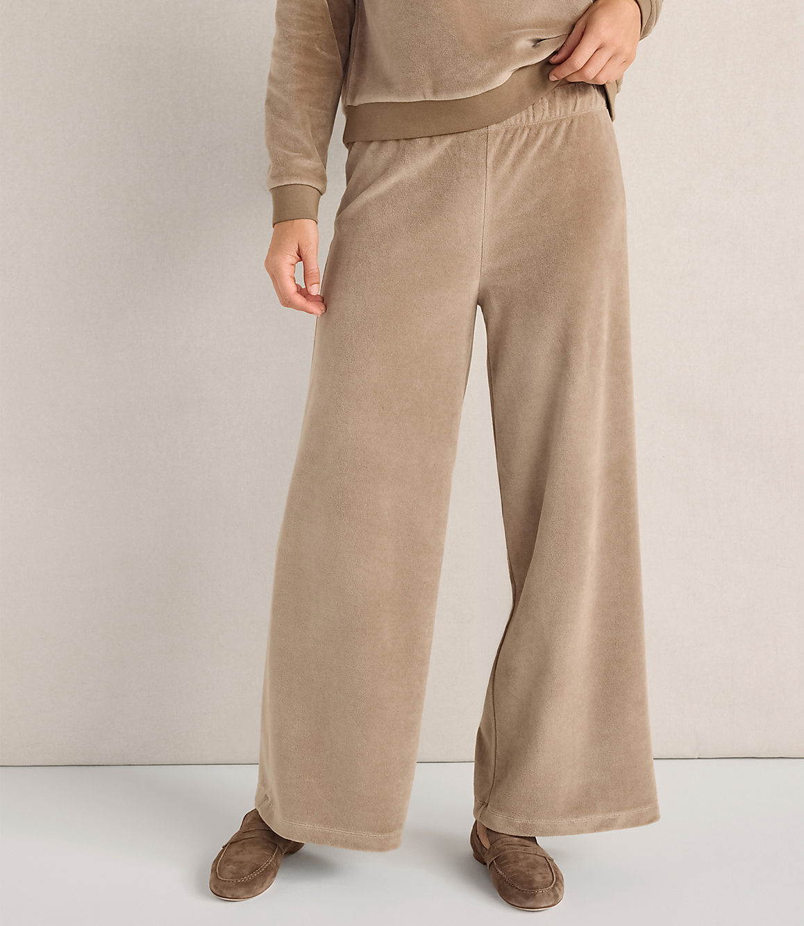 A person wears tan velvet wide-leg pants and a matching top against a plain, neutral-colored wall.