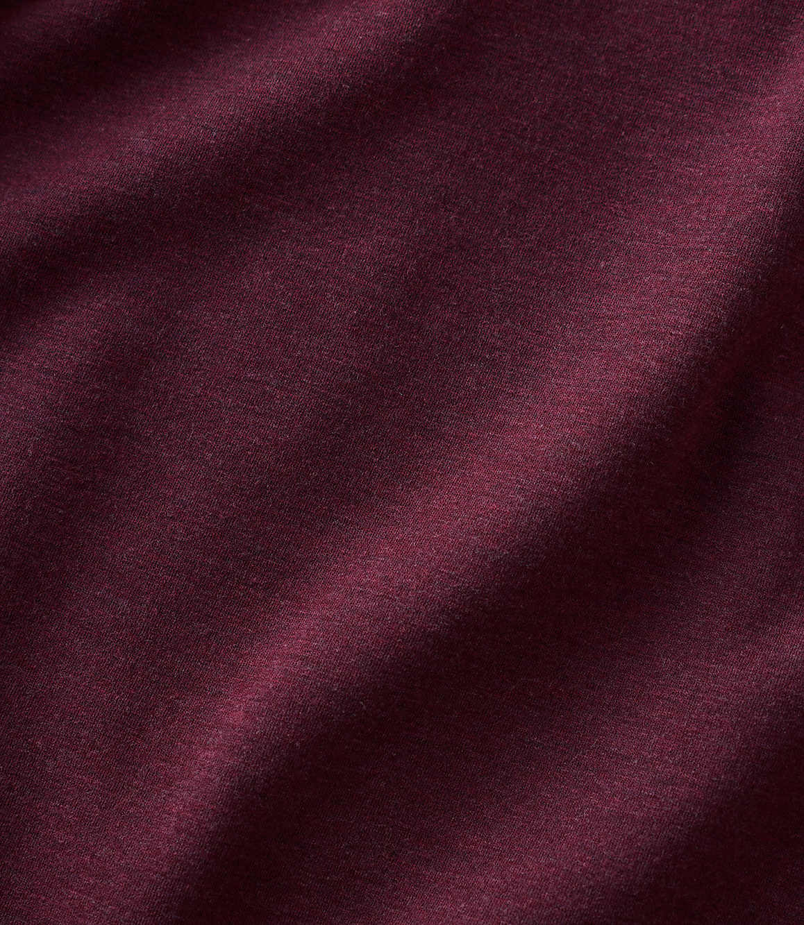 A close-up of maroon fabric with soft folds in the foreground and a slightly blurred texture in the background.