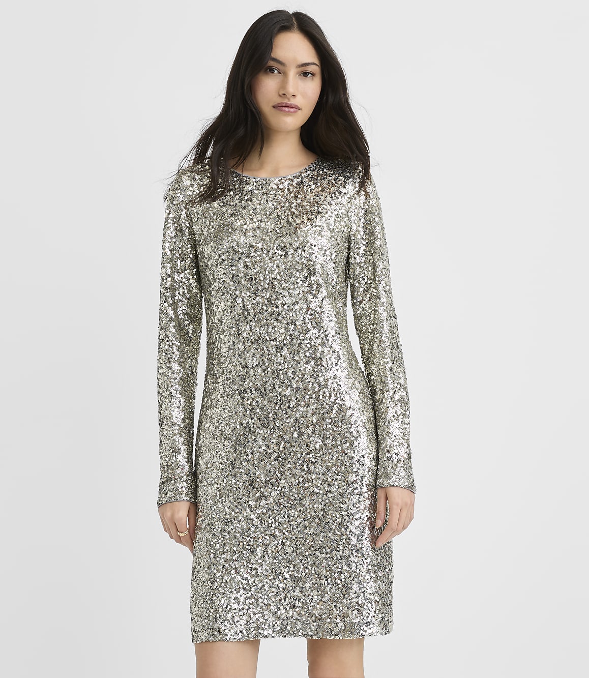 A woman wearing a long-sleeved silver sequin dress stands against a plain white background.