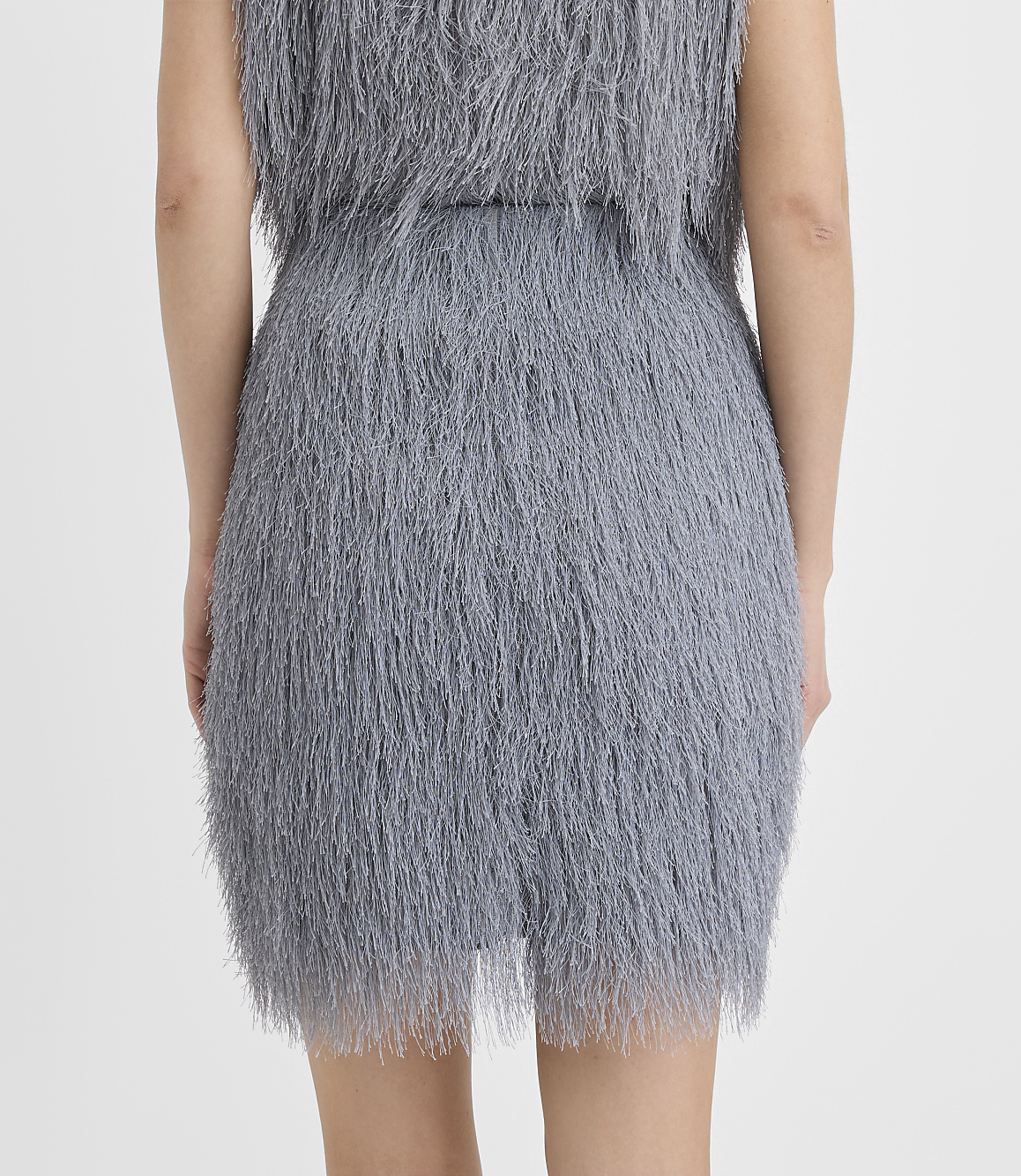 A person is seen from behind wearing a grey shaggy faux-fur dress against a plain white background.