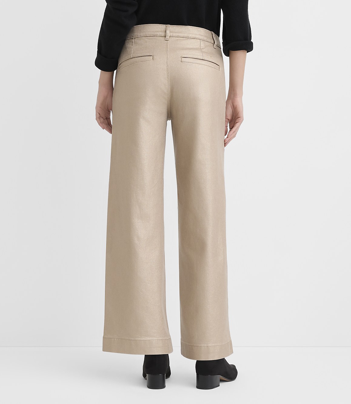 A person wearing a black top, wide-leg beige trousers, and black heels stands against a plain white background.